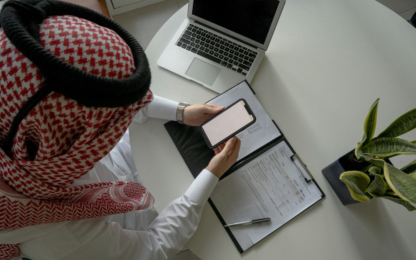 A man in a ghutra using a banking app at his desk