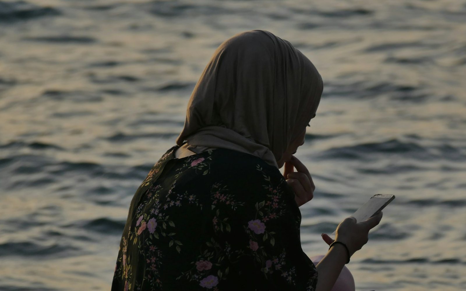 A woman checking her phone by the water at dusk